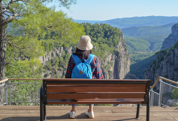 A woman traveling through the mountains of Turkey with a backpack sits on a bench on the edge of the Tazi Canyon and admires the mountains, a girl outdoors enjoying the view of the Tazi Canyon
