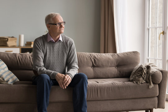 Hoary loneliness and sadness. Pensive melancholic older man feel abandoned lonely at home sit on couch stare into distance with upset look struggle with crisis of aging miss days of youth. Copy space