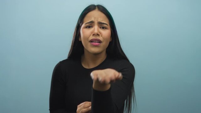 Woman holds her hand in a begging pose with background showcasing a young latin hispanic individual against an isolated blue wall.