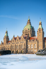 Obraz premium Das neue Rathaus der Landeshauptstadt Hannover im Winter bei blauem Himmel und Sonnenschein, im Vordergrund der Maschteich mit Eis und Schnee (Hochformat)
