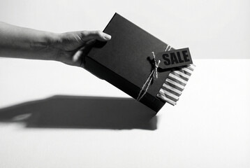Hand dropping a matte black gift box onto a white surface, dramatic hard shadow, striped tissue paper peeking out