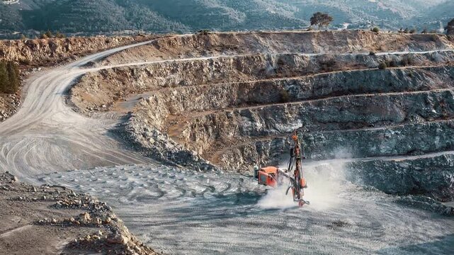 Heavy drilling machine operating at open pit stone quarry. Industrial mining equipment creating dust during excavation process. Panning wide shot.