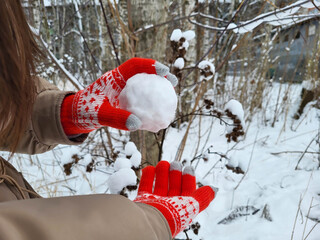 Winter fun on vacation. Hands wearing red gloves are preparing to throw a round white snowball.