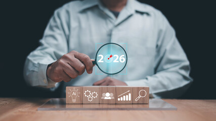Future business strategy concept. Hand holding magnifying glass with 2026 target and wood block with AI, data analysis, growth planning and innovation icons. Modern vision for corporate development.