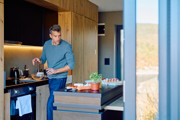 Man mixing ingredients in a bowl, preparing a healthy breakfast in a well-lit modern kitchen with...