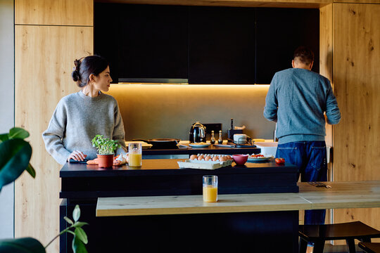 Couple experiencing relationship conflict and ignoring each other during breakfast preparation in a modern home kitchen - Powered by Adobe