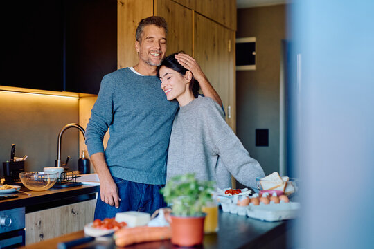 Loving couple standing together in a modern kitchen, sharing a tender moment and preparing breakfast at home