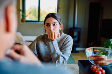 Woman listening closely to another person, hand to chin, showing pensiveness and concern during an important discussion at home