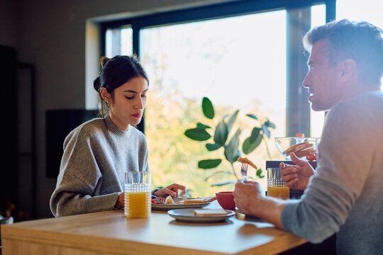 Couple having a difficult conversation during breakfast. Woman looking sad and man talking during a relationship conflict - Powered by Adobe