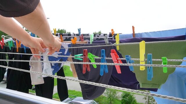 Laundry hanging on clotheslines outside window. Close view of colorful clothespins and clothes drying on balcony lines, hand reaching out, urban outdoor home routine.