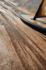A close-up of wet sand with a windsurfing board resting on it, leaving distinct tracks, suggesting a recent ride and active leisure.