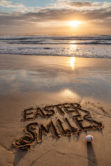 Easter Smiles Handwritten in Wet Sand with Gentle Waves and Small Pastel Egg, Vertical Layout with Copy Space &ndash; perfect for Easter promotions
