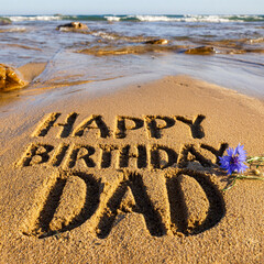 Happy Birthday Dad Block Letters Pressed in Wet Sand with Blue Cornflower and Golden Sunset Horizon &ndash; perfect for birthday greetings