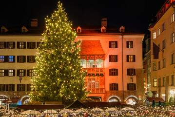 Tall illuminated Christmas tree at Christmas market in a square surrounded by historic buildings at night. Innsbruck, Austria.