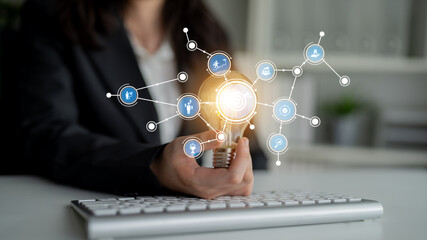A business person holds a glowing light bulb, representing innovation, surrounded by various idea...