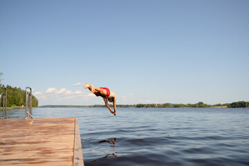 Fit man in swimwear dives off pier into lake. Bold movement and expression of strength.