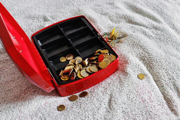 Open red cash box on textile bed blanket with scattered coins
