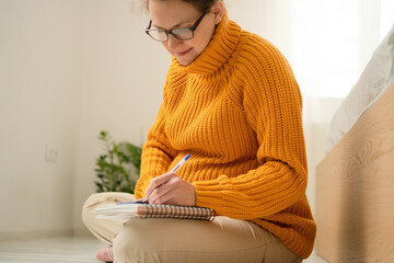 Expecting mother thoughtfully writing important delivery notes in her journal. Warm domestic scene of maternity preparation and organization.