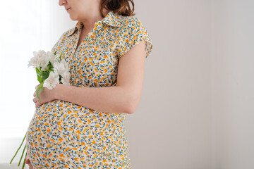 Expecting mother cradling white flowers while lovingly touching her baby bump. Pregnant woman
