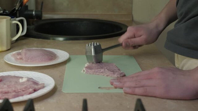 Home kitchen preparing pork with hammering techniques, Closeup of hands aggressively tenderizing pork on kitchen board, Focused home cook using meat tenderizer to prepare pork with rhythmic impact
