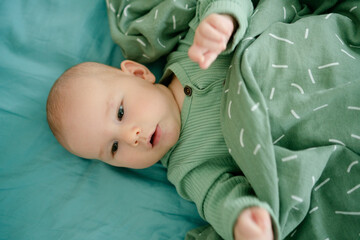 A smiling baby wrapped in a soft green blanket, radiating comfort and security, showcasing the importance of warmth and tenderness in a babys daily routine.