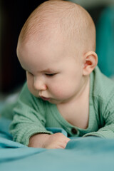 A baby in a ribbed green onesie rests on a soft blue blanket, showcasing an attentive expression that highlights the cozy atmosphere and gentle textures of a peaceful moment.