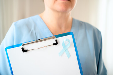 Close up of a woman doctor in medical uniform holding clipboard with blank paper and blue ribbon symbol for prostate cancer awareness and prevention in November health campaign