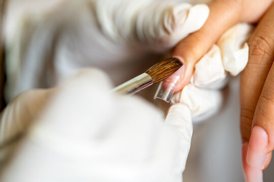 Manicurist applying acrylic nail extension on client finger