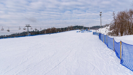 Groomed ski slope with a chairlift and blue safety netting at a mountain resort in winter