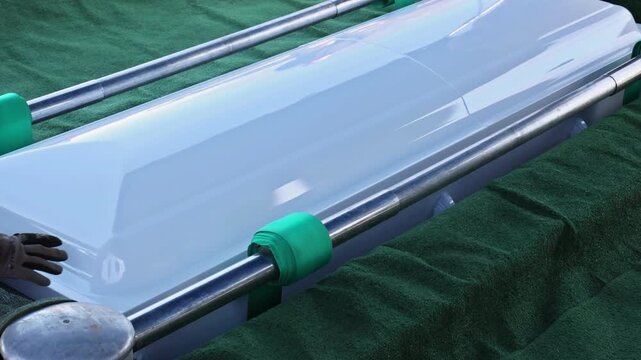 Funeral casket positioned on green drape with metal holders at cemetery service