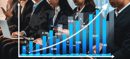 Business professionals in suits engage with mobile devices while analyzing a graph depicting substantial growth, highlighting teamwork and modern technology in a corporate environment. Amity