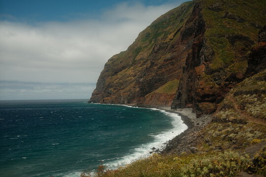 Dramatic Coastal Cliffside with Turquoise Ocean Waves and Rocky Shoreline on Cloudy Day