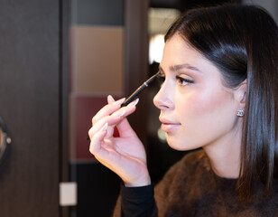 Obraz premium Young woman carefully applying eyebrow pencil, shaping and filling her eyebrows, focusing on achieving a natural and defined look during her daily makeup routine
