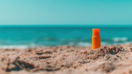 Sunscreen bottle on sand with ocean and blue sky in background
