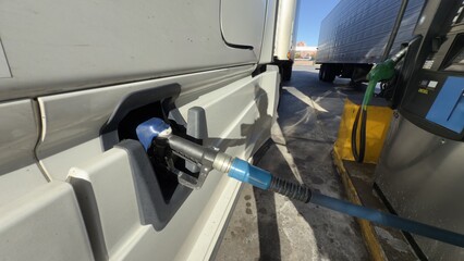Fototapeta premium Macro shot of a high-flow fuel nozzle inserted into a truck's diesel tank during refueling. Bright sunlight highlights the metal textures. Concept of logistics, energy, and transportation.