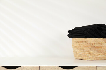 Laundry basket with clothes on table near white wall indoors, closeup. Space for text