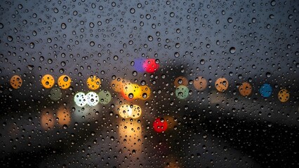 Close up view of heavy raindrops hitting a car window, with blurry traffic lights and urban street scenes visible in the background