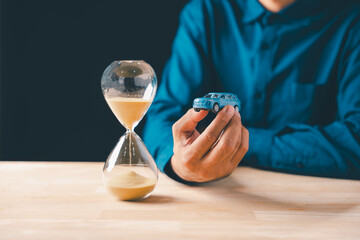 Individual holds car, hourglass shows time passing, symbolizing finance, loan, and saving money, crucial for understanding car cost, insurance, and depreciation for business