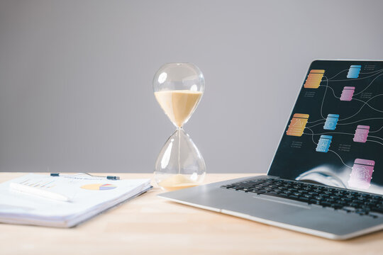 Hourglass for work, time management essential for business documents, paperwork on desk with laptop displaying data, emphasizing modern file organization and business efficiency - Powered by Adobe