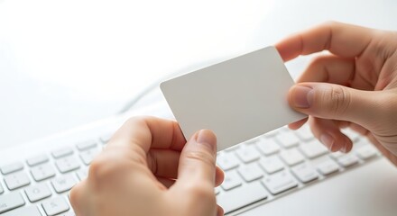 Hands holding a blank white card over a computer keyboard, suggesting online transactions or digital identity.