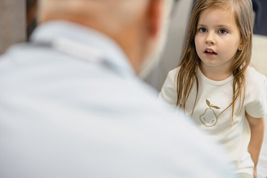 Young girl sitting on the examination bed looking at the male doctor