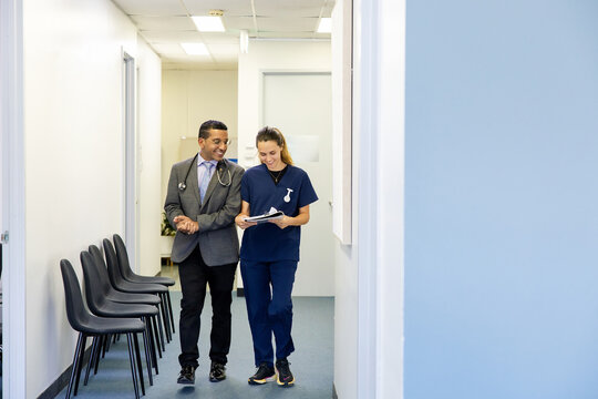 Doctor and nurse talking while walking down office hallway