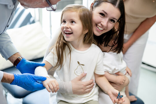 Young girl looking up to the doctor wrapping her arm with white bandage