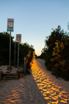 signs along path to beach with sunset light on sand