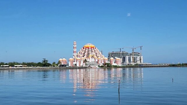 The iconic 99 Domes Mosque (Masjid 99 Kubah) stands prominently on the reclaimed waterfront of Losari Beach, featuring its signature orange and white architectural design under a bright daylight sky.