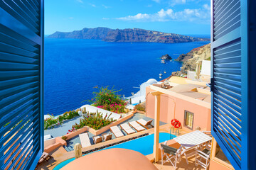 Sea view past blue window shutters of pastel and whitewashed terraces and houses at the idyllic Greek village of Oia, on the island of Santorini, Greece.