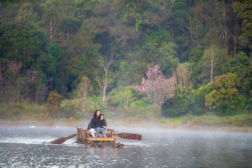 Pang Ung or Pang Tong Reservoir with family tourists travel rafting in lake with white swan and nature tiger claw tree or pink cherry blossom and morning fog mist on water surface in winter Thailand