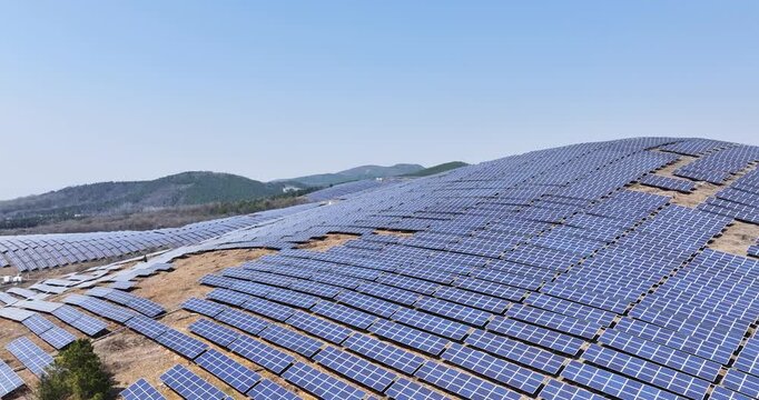 Aerial video of a vast solar power station on hilly terrain, featuring rows of photovoltaic panels under a clear blue sky, symbolizing renewable energy and sustainable development.