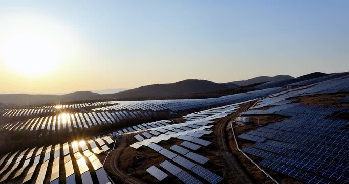 Aerial footage of a large-scale solar farm on hills at sunset, with rows of photovoltaic panels reflecting golden light, sustainable development and clean energy landscape