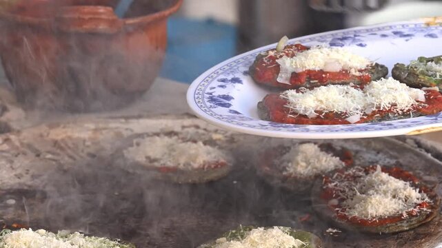 Authentic Mexican gastronomy, preparing corn tortillas with salsa and cheese, memelas on a traditional clay griddle